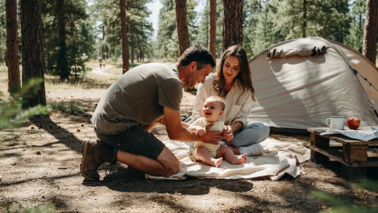 Parents with a baby at a sunny campsite beside a tent