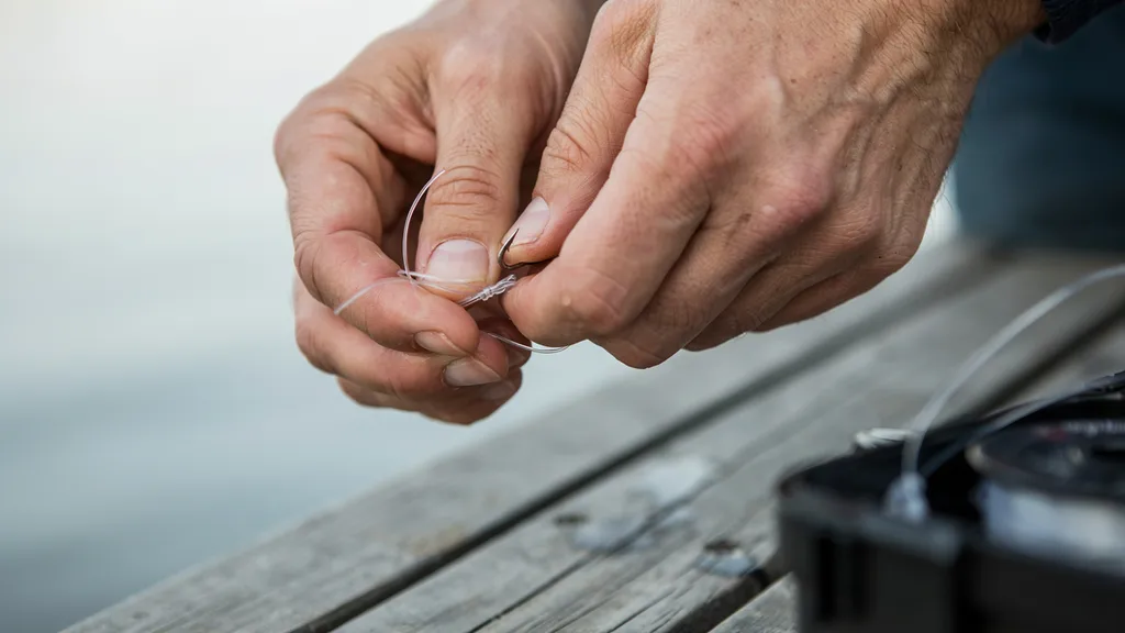 Hands tying a fishing knot on a hook with monofilament line