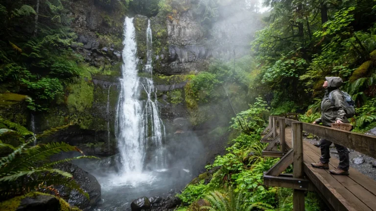 A tall waterfall in a lush forest with a viewing platform