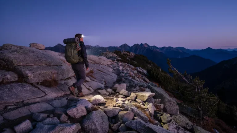 Hiker wearing a glowing LED headlamp at dusk on a mountain trail