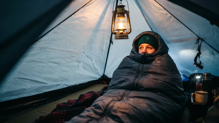 Camper snug in a sleeping bag with beanie inside a frosty tent